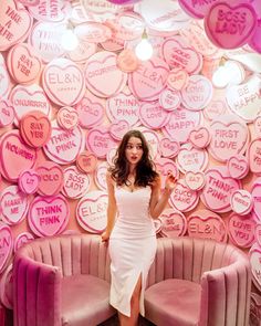 a woman in a white dress standing next to pink chairs with hearts on the wall