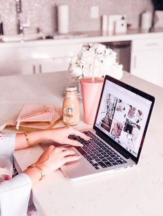 a woman is typing on her laptop at the kitchen counter with flowers in vases