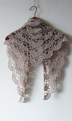 a crocheted shawl hanging from a hook on a white wall with a wooden hanger