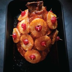 pineapples and cherries are arranged in the shape of a heart on a black plate