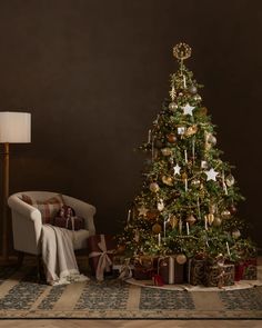 a decorated christmas tree in a living room next to a chair with presents under it