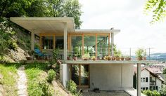 the house is built on top of a steep hill with plants growing from it's balconies