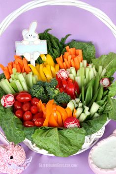 a basket filled with lots of fresh vegetables on top of a purple tablecloth next to other food items