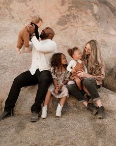 a group of people sitting next to each other on top of a rocky hill with one woman holding a baby