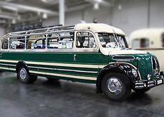 an old green and white bus is parked in a garage with other vehicles behind it