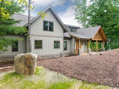 a house in the woods surrounded by trees and grass with a large rock on the ground