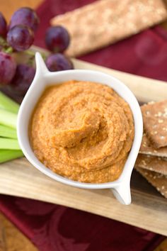 a bowl of hummus and crackers on a cutting board next to some grapes