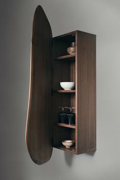 a wooden shelf with bowls and plates in it next to a wall mounted surfboard