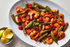 a white plate topped with shrimp and vegetables next to a bowl of lemon wedges