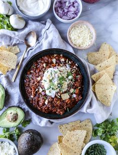 a bowl of chili with tortilla chips and avocado on the side