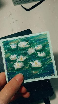 a person holding up a small card with water lillies on the water in it