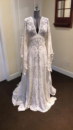 a white wedding dress on display in a room with a mirror and window behind it