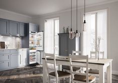 a white table and chairs in a room with wooden flooring, blue cabinets and an open refrigerator