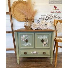 an old dresser painted in green with flowers and leaves on the top, next to a wicker basket