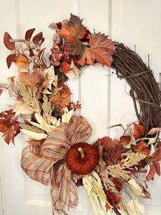 a wreath with fall leaves and pumpkins hanging on a door