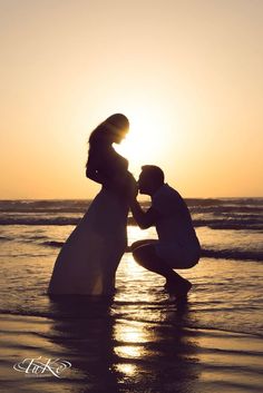 a man kneeling down next to a woman on top of a beach near the ocean