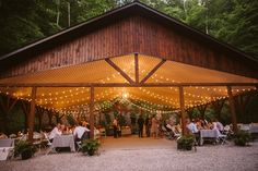 an outdoor wedding venue with lights strung from the roof and people sitting at tables under it