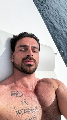 a shirtless man laying on the back of a boat with his arm around him