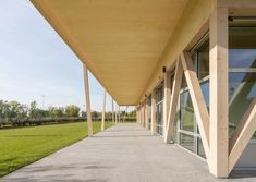 an empty walkway between two buildings with large windows on each side and grass in the background