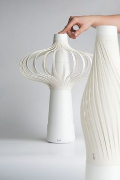 a hand is touching the top of a white vase with wavy lines on it's sides