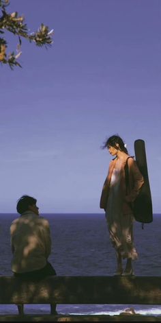 two people sitting on a bench looking at the ocean