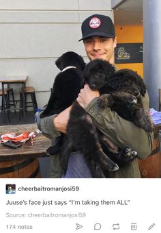 a man holding two puppies in his arms while standing next to a table with other dogs