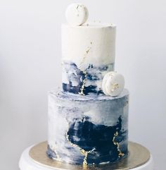 a white and blue cake with gold sprinkles on the top is sitting on a stand