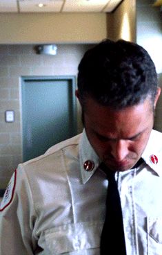 a man in uniform looking down at his cell phone while wearing a tie and white shirt