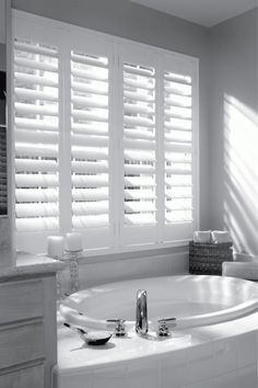 a white bath tub sitting next to a window with shutters on the windowsill