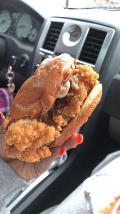 a person holding up a chicken sandwich in their hand while sitting in the backseat of a car