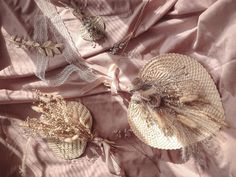 three decorative items are laying on a pink satin sheet with lace and feathers attached to them