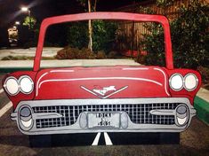 an old red car painted on the side of a parking lot at night with its hood up