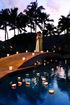 a bride and groom standing next to a pool with floating candles