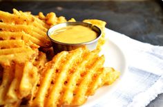 a white plate topped with cheesy fries and dipping sauce