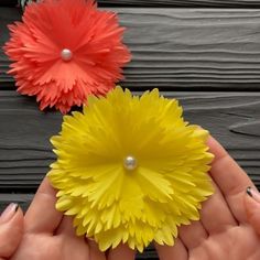 two paper flowers are being held by someone's hands on a wooden surface with pearls