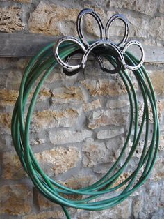 a bunch of green hoses hanging on a brick wall next to a stone wall