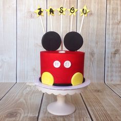 a mickey mouse cake on a pedestal with the word reason spelled out in yellow letters