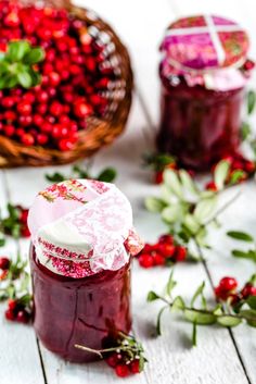 cranberry jam in a jar with fresh berries around it on a white wooden table