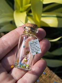 a person holding a tiny glass bottle with flowers in it and a message on the inside