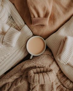 a cup of coffee sitting on top of a bed covered in blankets and sweaters