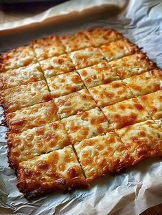 a square piece of cheese pizza sitting on top of a white sheet of wax paper