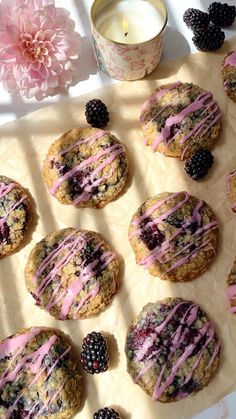 blackberry cookies with pink icing and blackberries on parchment paper next to a candle