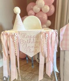 a pink and white birthday party with balloons in the background, including a baby's crib