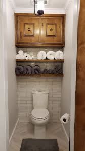 a white toilet sitting inside of a bathroom next to a wooden shelf filled with rolls of toilet paper