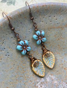 Beautiful turquoise blue flower beads are Czech glass. They have a bronze wash highlighting the details. I hand wrapped neutral ivory and pale blue Czech glass leaves in antique brass wire to hang from the flowers.   Hooks are 100% brass with an antique finish. They are nickel free. Lever back hooks are available upon request.  These nature inspired boho earrings make a great gift for the flower loving girl in your life. Dress them up with an airy spring dress or wear them with your favorite blu Simple Bead Earrings, Vintaj Jewelry, Czech Beads Jewelry, Glass Flower Earrings, Czech Glass Jewelry, Ears Pierced, Handmade Boho Jewelry, Earrings Nature, Lampwork Jewelry