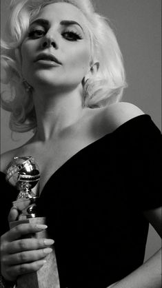 a woman with blond hair holding a golden globe in her right hand and looking off to the side