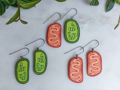 four earrings with different designs on them sitting next to some green and orange leaves in the background