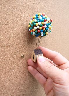 a hand holding a tiny wooden house with candy on it's back and a balloon attached to the wall