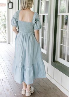 a woman in a blue dress is standing on the porch with her back to the camera