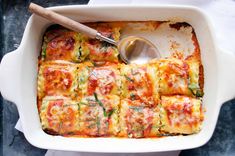 a casserole dish with cheese and spinach in it, next to a spoon